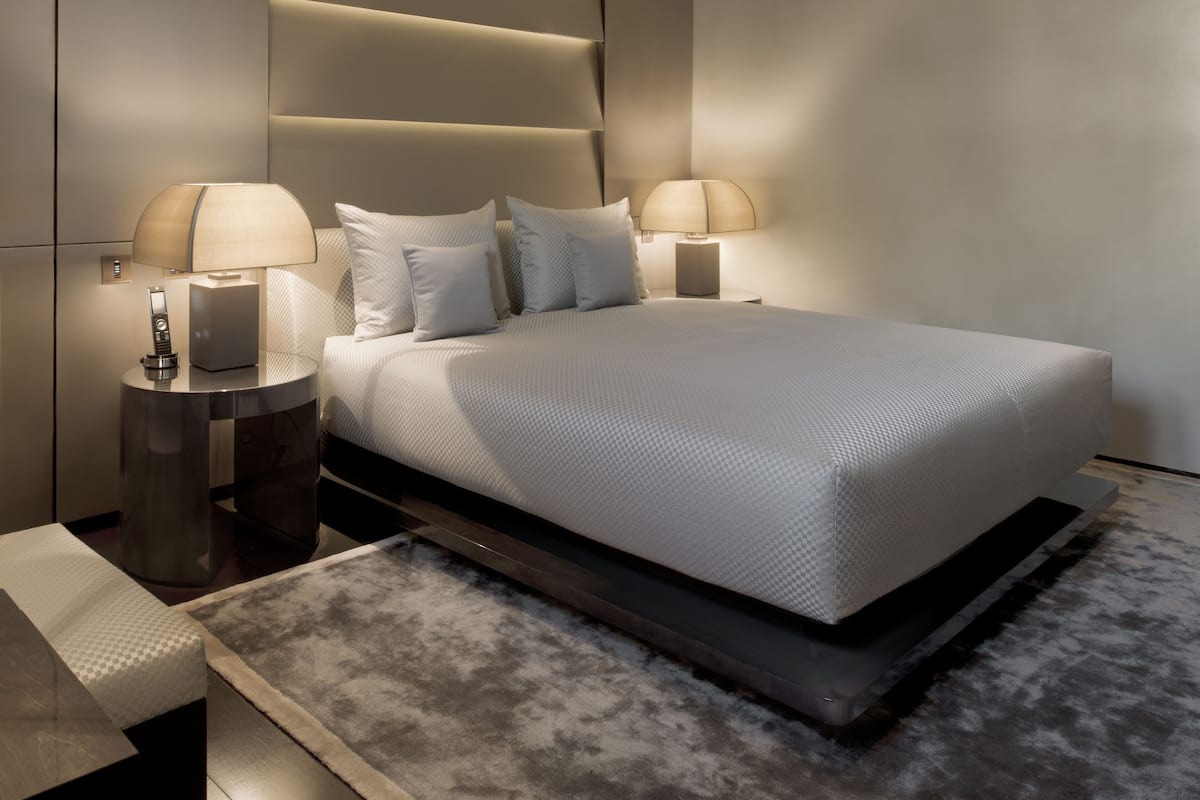 A modern bedroom with a large bed, two bedside tables with lamps, and a built-in headboard.