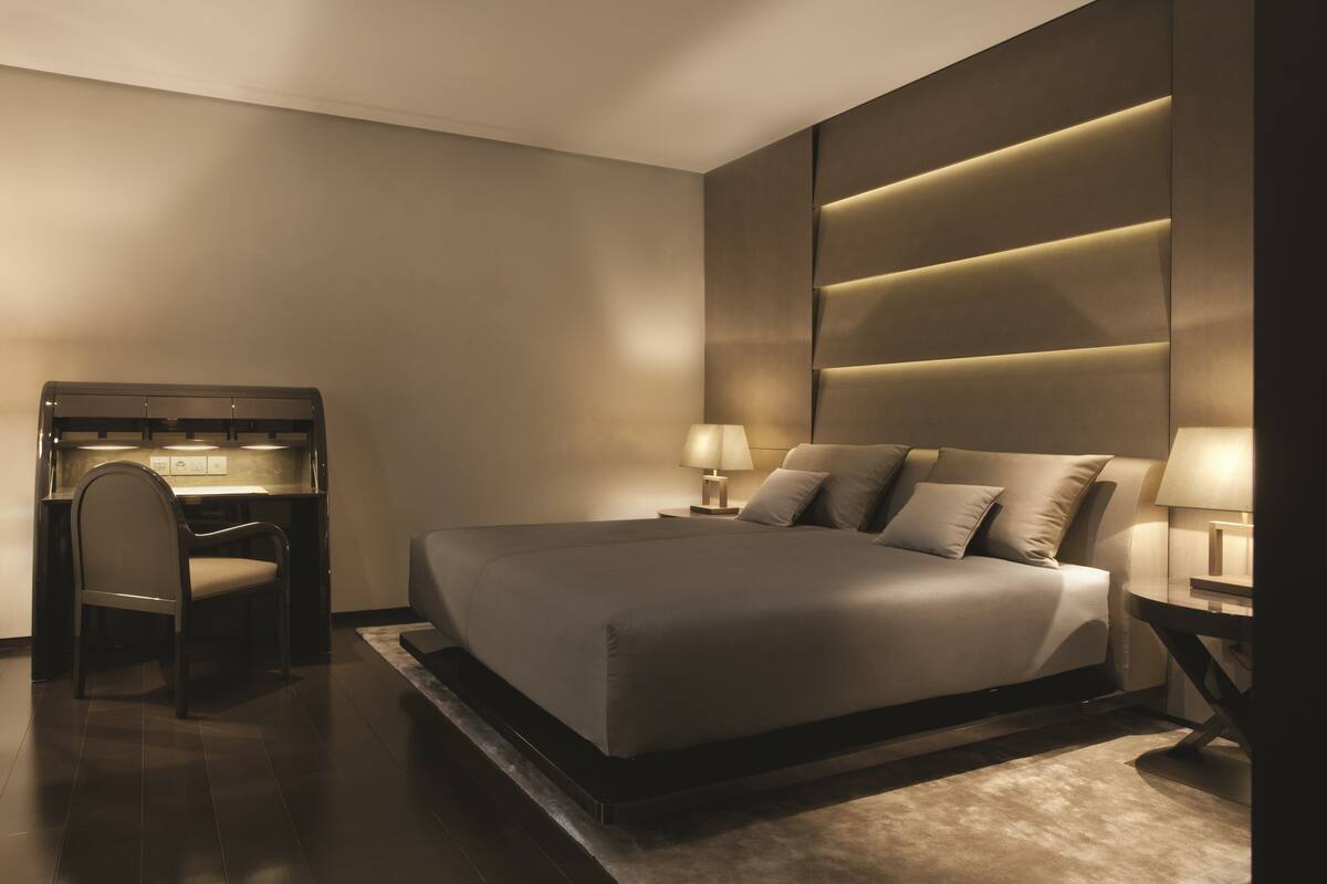 A modern bedroom with a large bed, bedside lamps, a desk, and a chair.