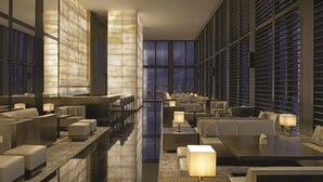 Un moderno vestíbulo de hotel con área de bar, espacios de descanso y grandes ventanales con vistas a la ciudad.