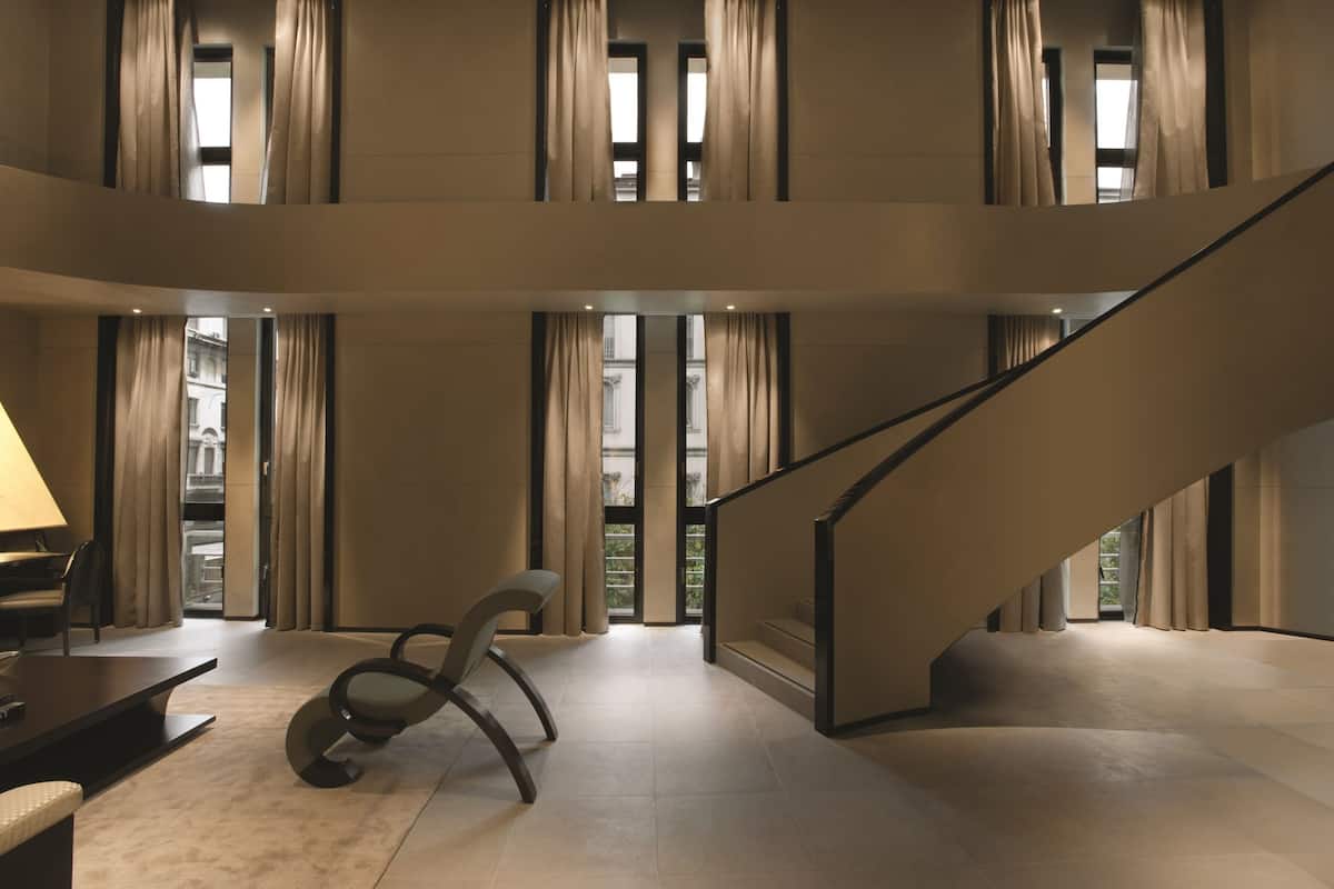 A spacious interior with a modern staircase, large windows with curtains, and a minimalist seating area.
