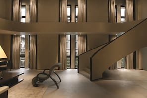 A spacious interior with a modern staircase, large windows with curtains, and a minimalist seating area.