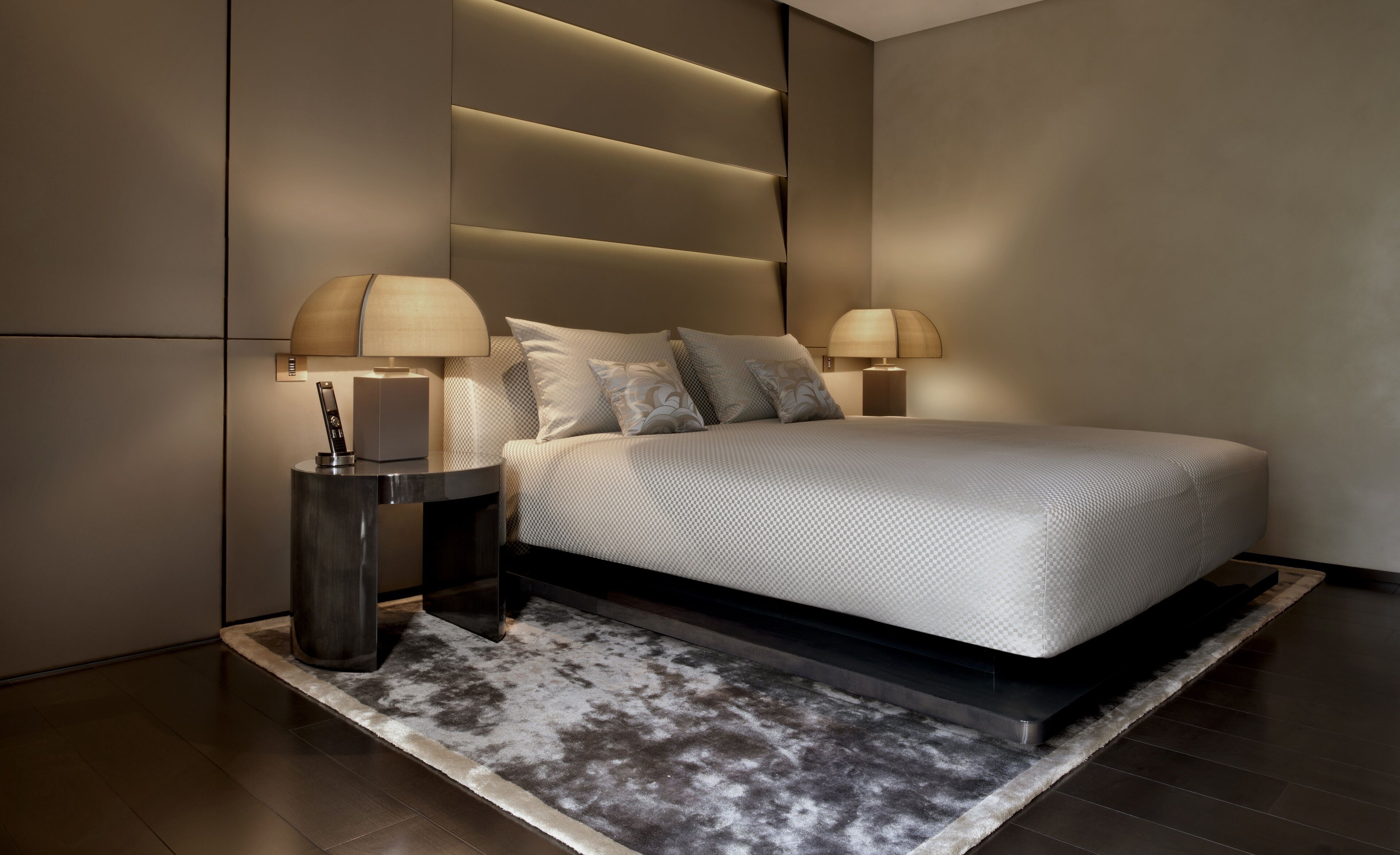 Ein modernes Schlafzimmer mit einem großen Bett, zwei Nachttischen mit Lampen, einem Teppich und einer wandmontierten Lichtleiste.