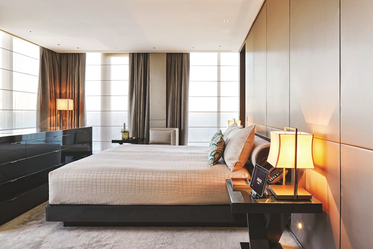 A modern hotel room with a large bed, a bedside table with a lamp, a TV, and a wardrobe.