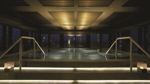 A modern indoor pool area with a glass ceiling, metal railings, and a view of the city at night. - Armani Hotel Milano (Milan)