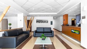A hotel lobby with a reception desk, black leather sofas, a glass coffee table with a bonsai, and a framed picture on the wall. - City Express Junior by Marriott Veracruz Aeropuerto (Veracruz)