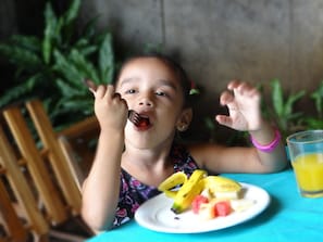 A child sitting at a table with a plate of fruit and a glass of orange juice.