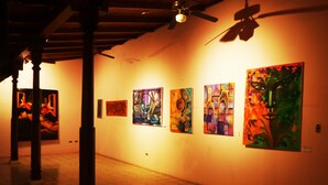 Een kunstgalerie met schilderijen aan de muren en een plafondventilator.