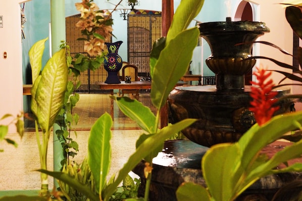 A room with a fountain, potted plants, and a traditional vase.