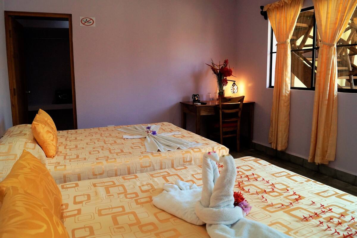 Une chambre d’hôtel avec deux lits, un bureau, une chaise, une lampe et une fenêtre avec des rideaux.
