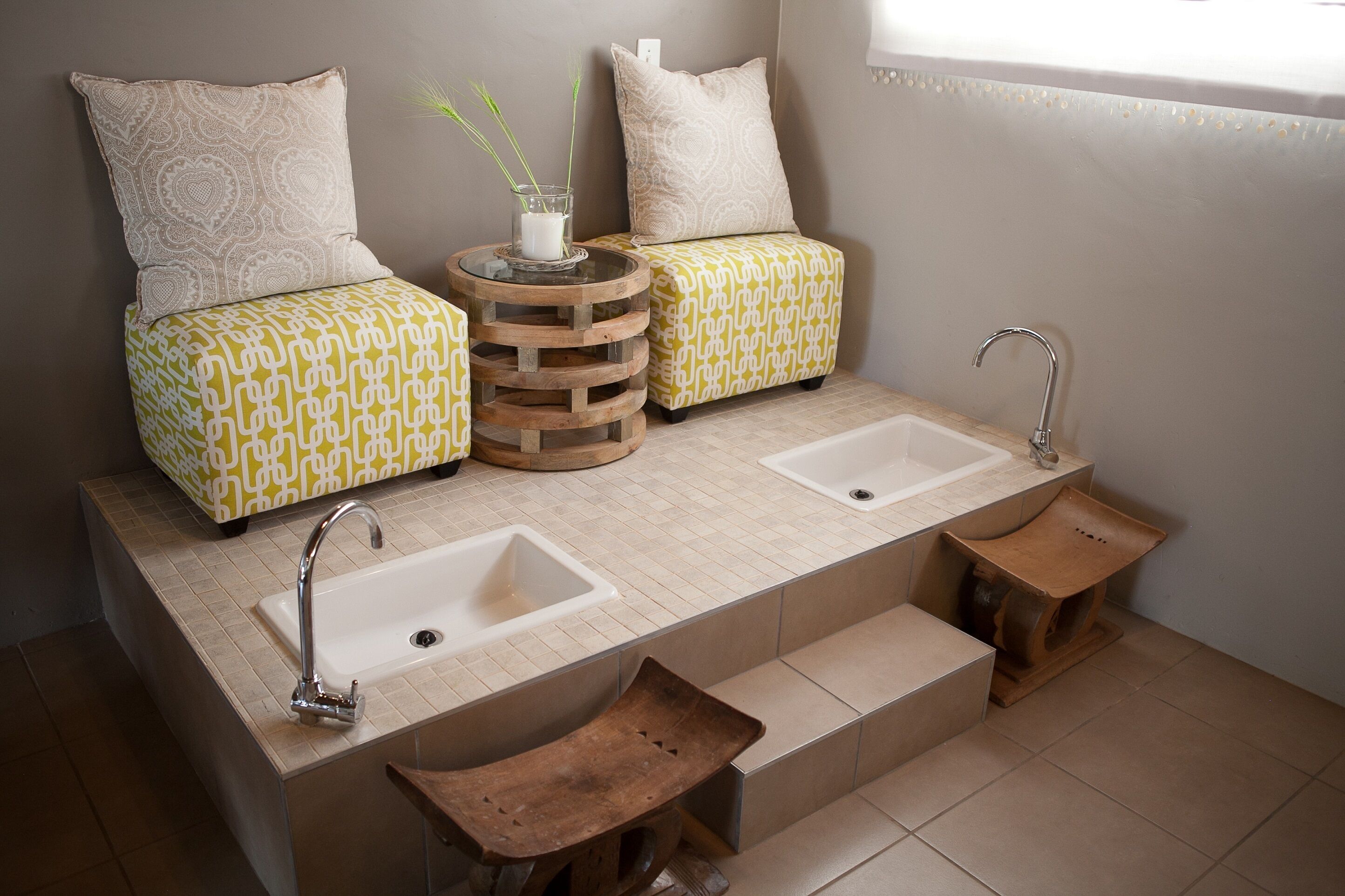 A bathroom with two sinks, a wooden stool, and patterned cushions.