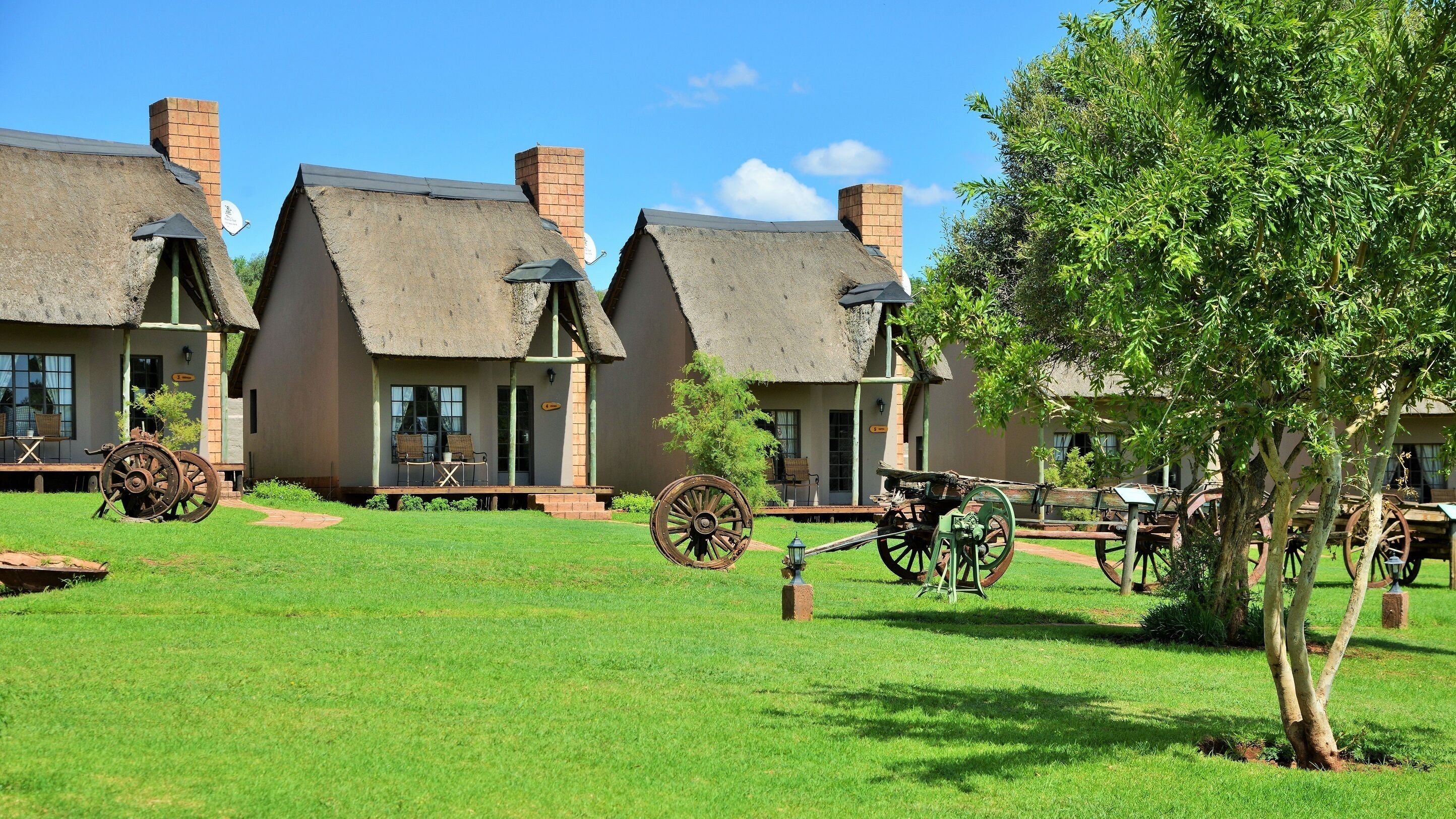 A traditional building with thatched roofs and brick chimneys, surrounded by a well-maintained lawn and historical farming equipment.