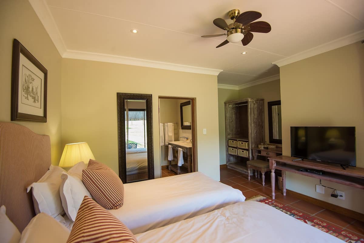 Une chambre d’hôtel avec un lit, un bureau avec une télévision, un ventilateur de plafond et une salle de bain visible à travers une porte ouverte.