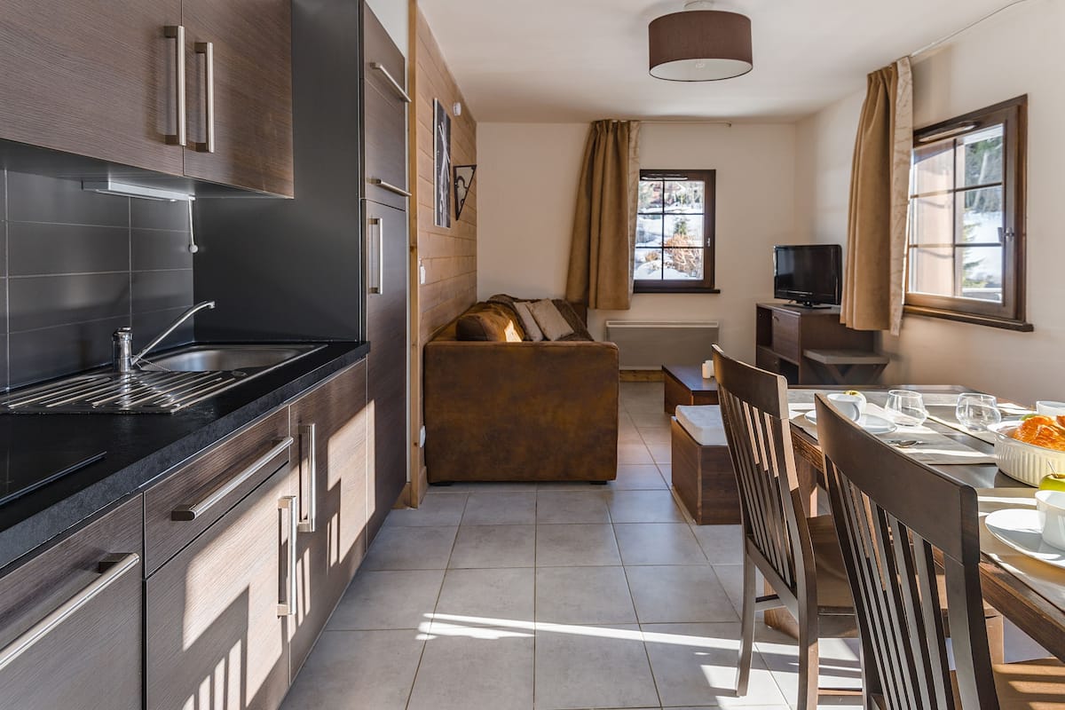 Una cocina moderna con estufa integrada, un comedor con mesa y sillas, y una zona de estar acogedora con un sofá.