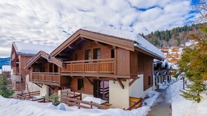 Eine Holzhütte mit einem Balkon, umgeben von verschneitem Gelände und Bäumen.