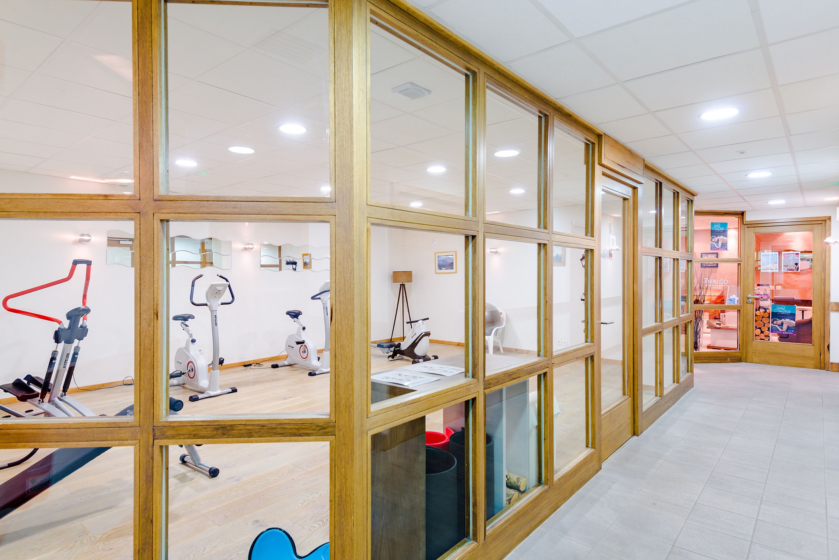A gym with exercise equipment, wooden-framed glass walls, and a tiled floor.