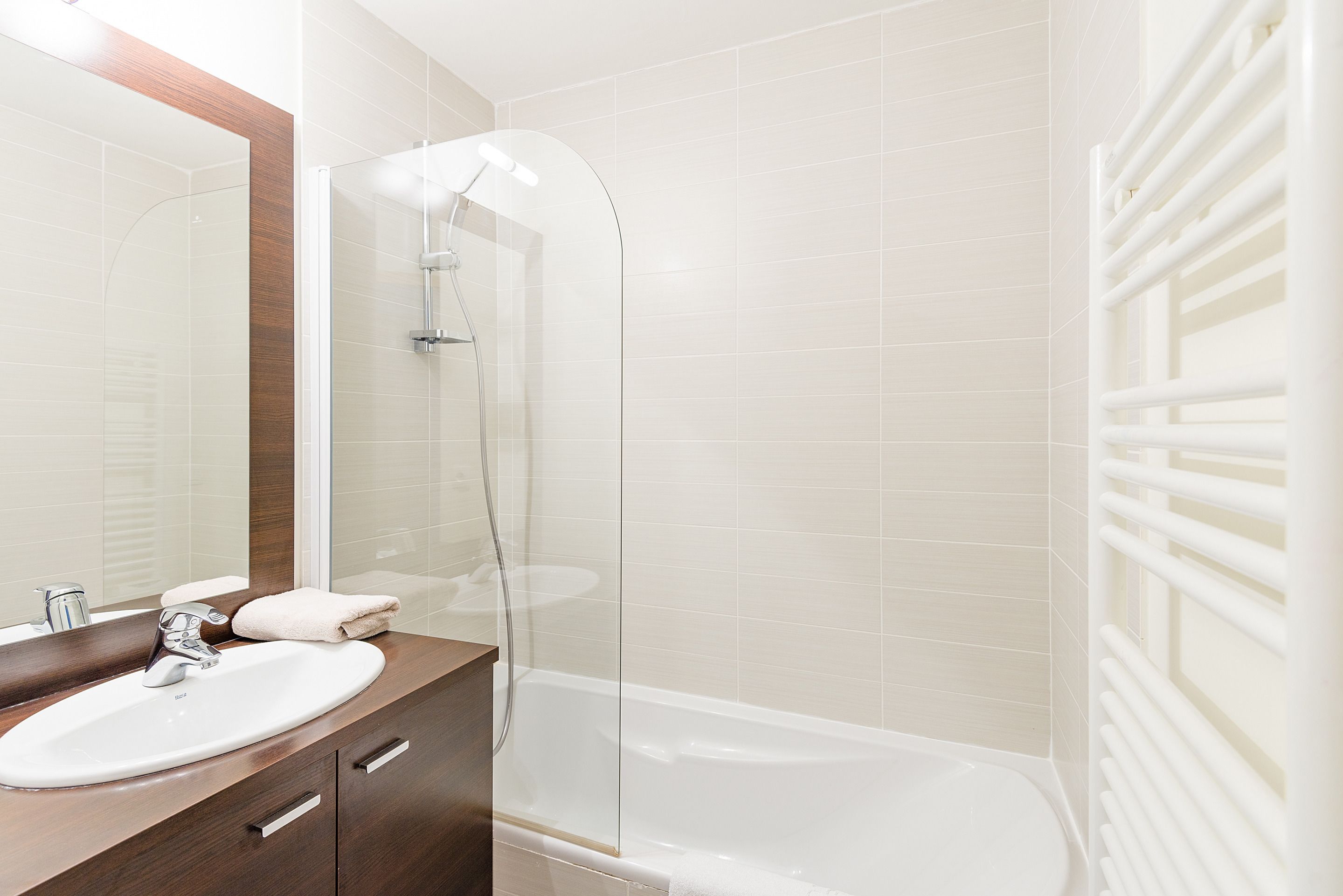 A modern bathroom with a glass-enclosed shower, a white bathtub, and a vanity with a mirror.