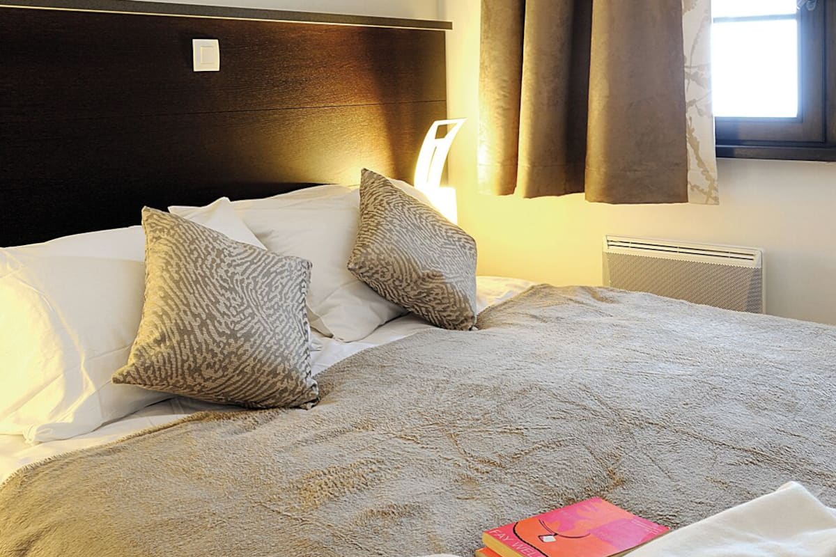Una cama bien hecha con cabecera, dos almohadas, una colcha y un libro sobre la cama.