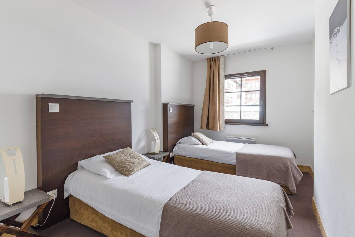 Habitación de hotel con dos camas, un escritorio, una lámpara y un ventanal con cortinas.