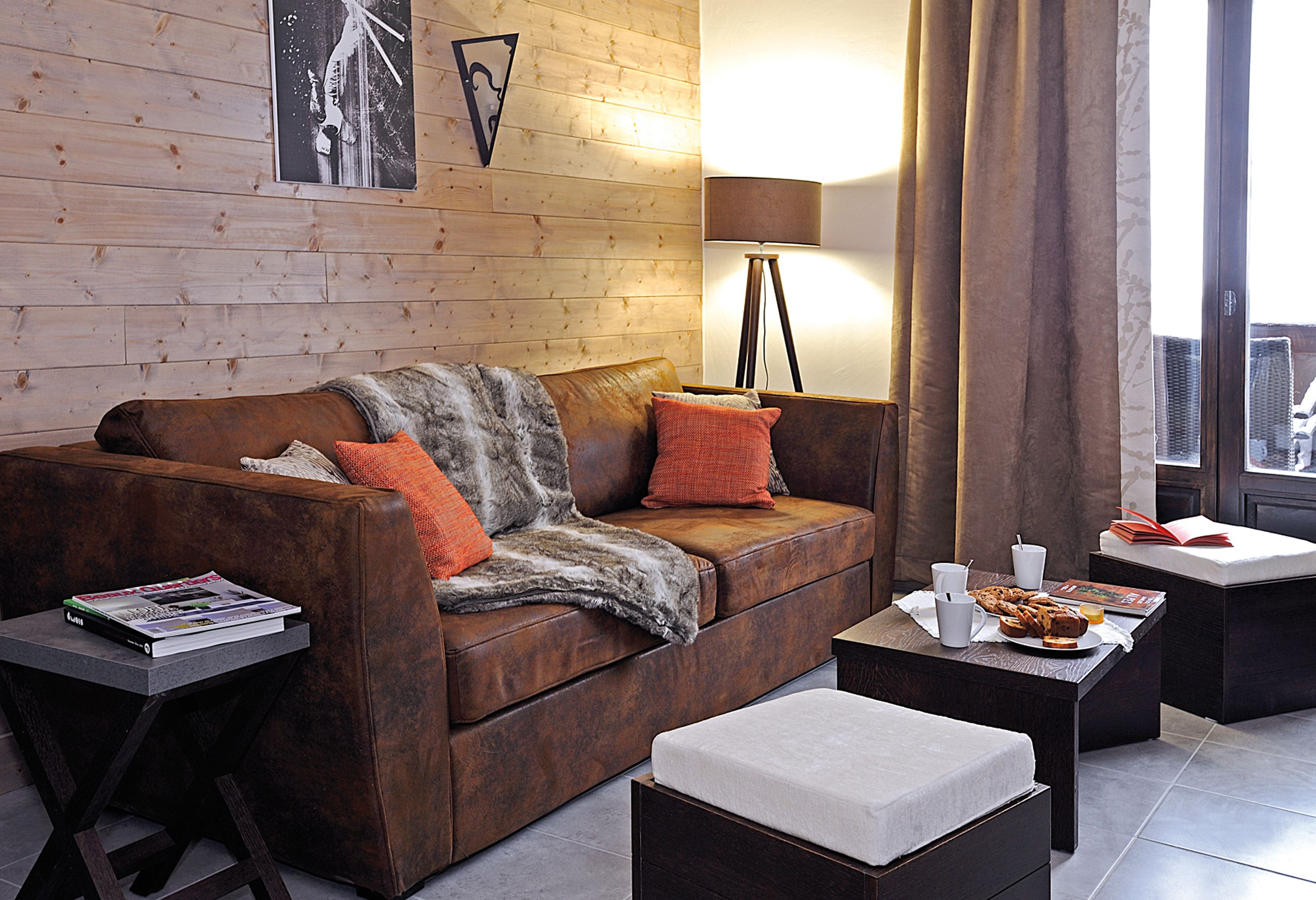 En moderne stue med en lædersofa, et sofabord med et magasin, et kaffebord med en tallerken mad og en gulvlampe.