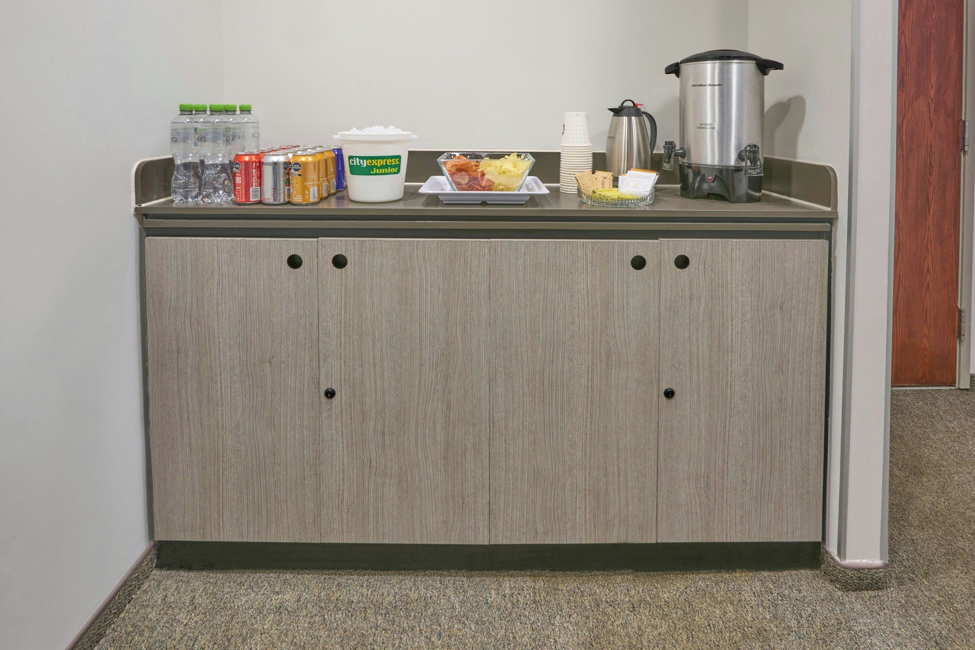 Una kitchenette con cafetera, dispensador de agua, un envase de yogur y una bandeja de comida.
