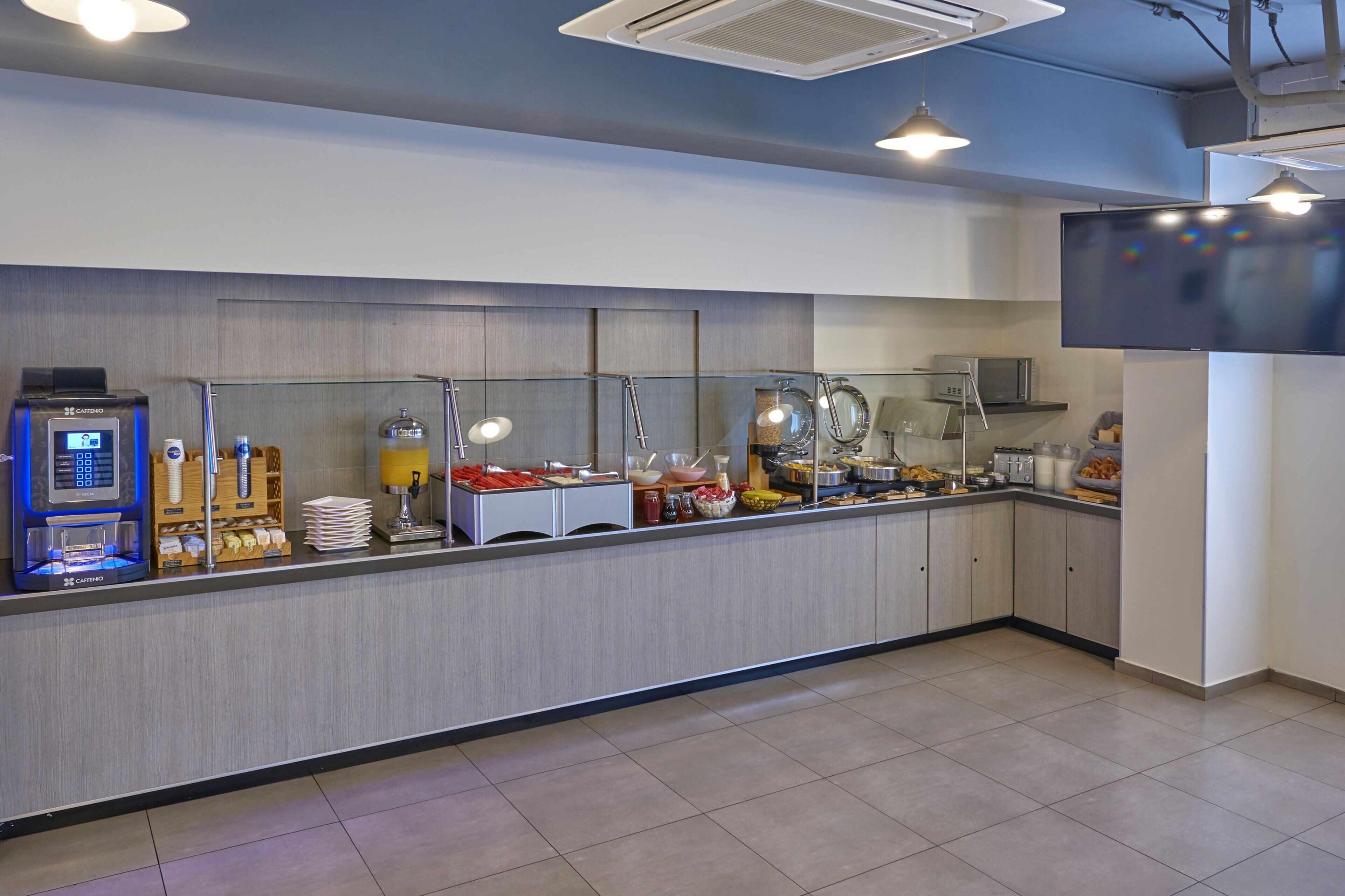 A modern breakfast bar with a coffee machine, glass display case, and various food items.
