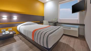 Ein Hotelzimmer mit Bett, Nachttisch, Lampe, Fernseher und Fenster.