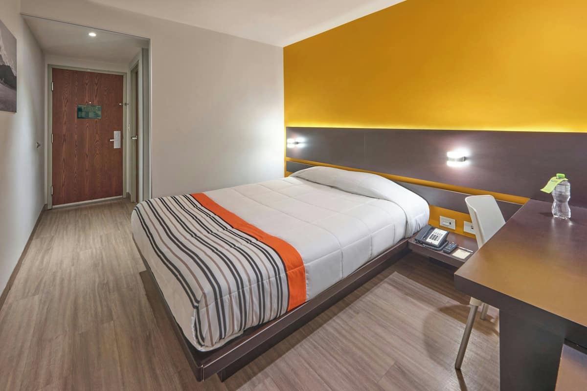 A hotel room with a bed, bedside table, chair, and a desk with a telephone.