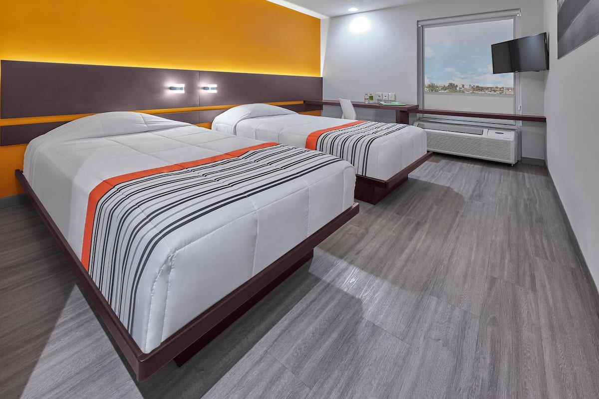 A hotel room with two beds, a TV, a desk, and a window with a city view.