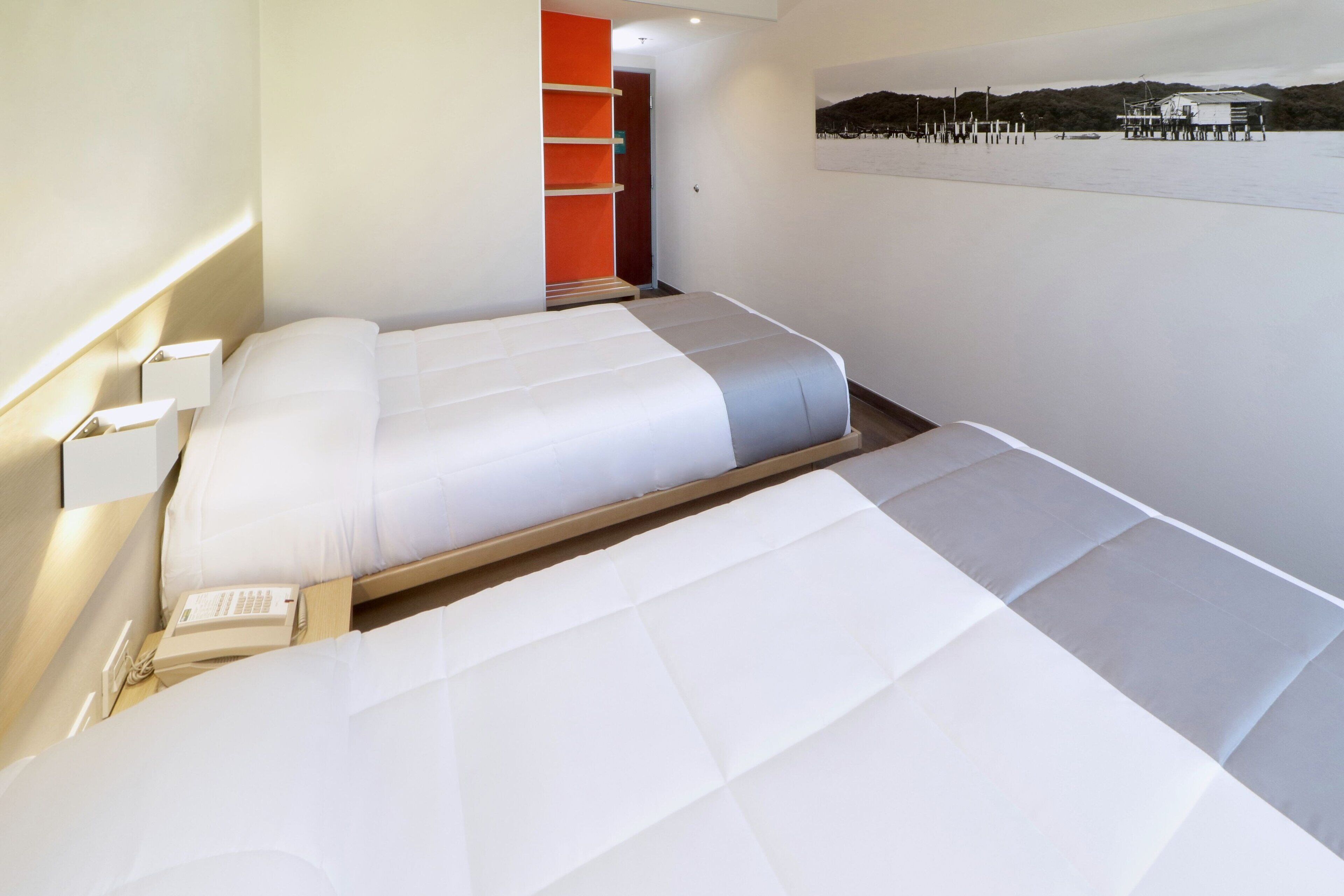 A hotel room with a bed, a bedside telephone, and a wall-mounted shelf.