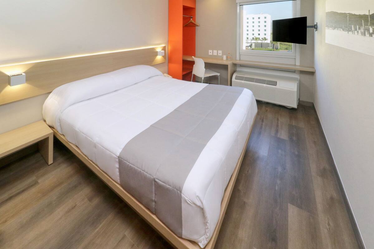 Une chambre d’hôtel moderne équipée d’un grand lit, d’un bureau, d’une chaise et d’un téléviseur fixé au mur.