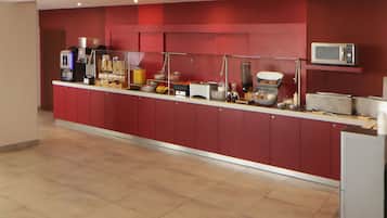 Un bufé de desayuno de hotel con una máquina de café, un microondas y diversas opciones de comida.