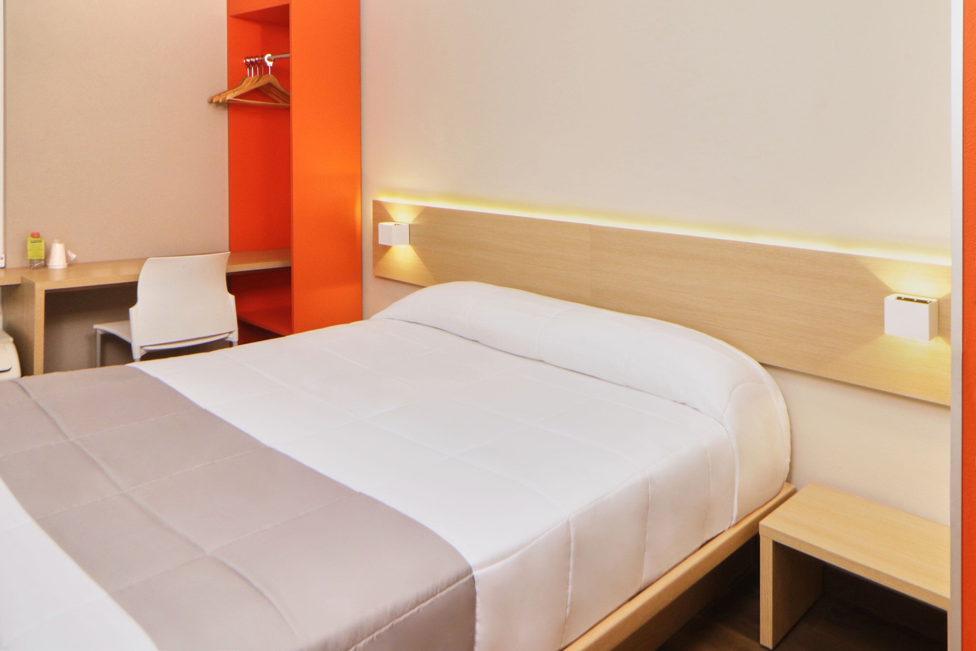 A hotel room with a bed, bedside table, and a desk with a chair.