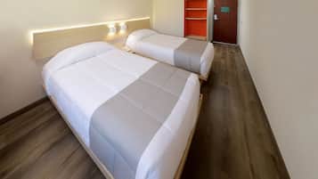 A hotel room with two beds, a wooden floor, a nightstand, and a wall-mounted light fixture.