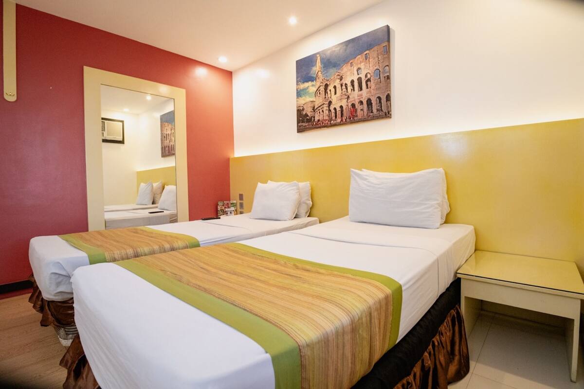 Une chambre d’hôtel avec deux lits simples, une petite table de chevet, un miroir et un tableau au mur.