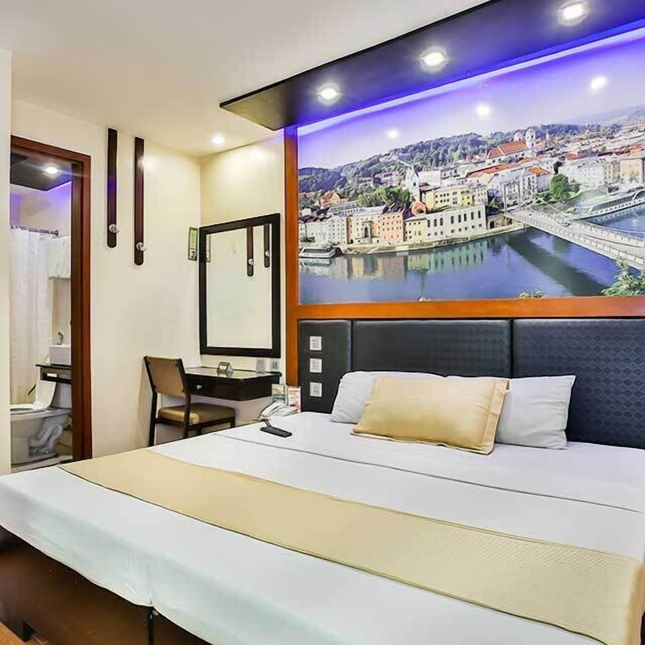 Een hotelkamer met een bed, een bureau en een stoel. Er is een groot raam met uitzicht op een stadsbeeld.