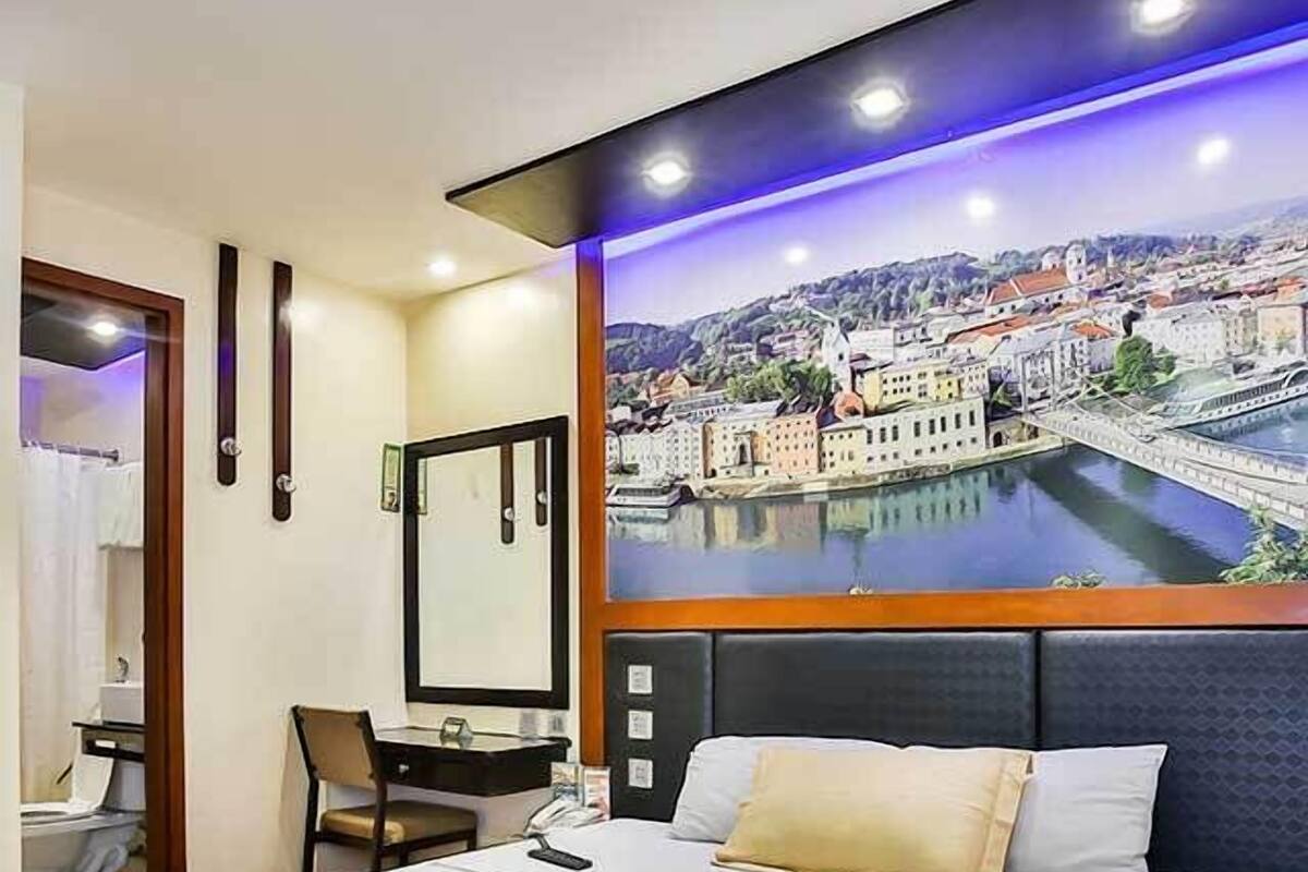 Une chambre d’hôtel avec un lit, un bureau et une chaise. Une grande fenêtre offre une vue sur le paysage urbain.