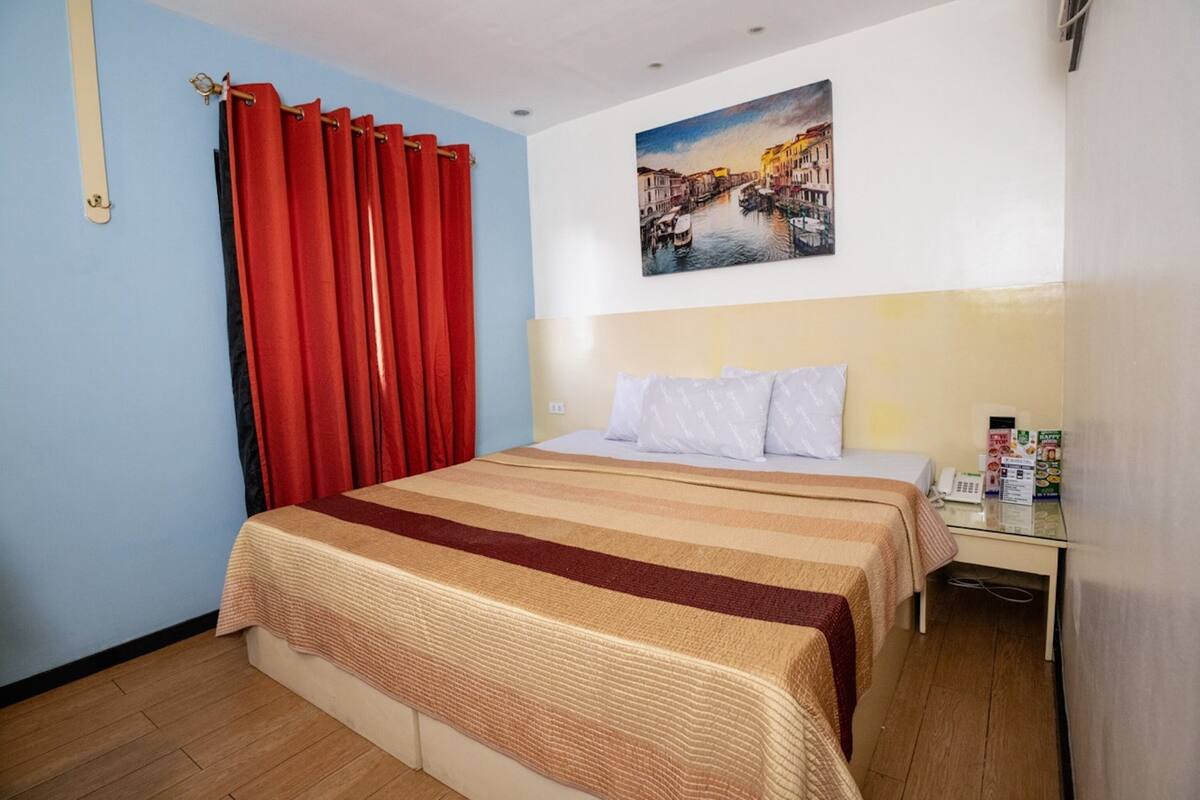 Une chambre d’hôtel équipée d’un lit, d’un bureau, d’un téléphone et d’un tableau représentant un paysage urbain.