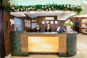 A reception desk with a marble counter, two staff members, a clock, and a decorative plant overhead. - Eurotel North Edsa (Quezon City)