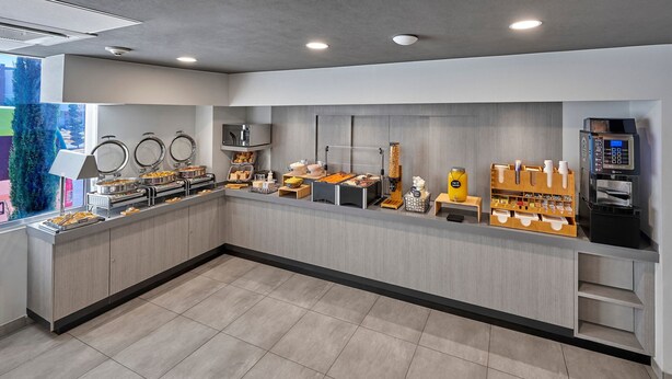 Een moderne ontbijtbar met bedieningsstations, inclusief koffieautomaten en diverse eetmogelijkheden.