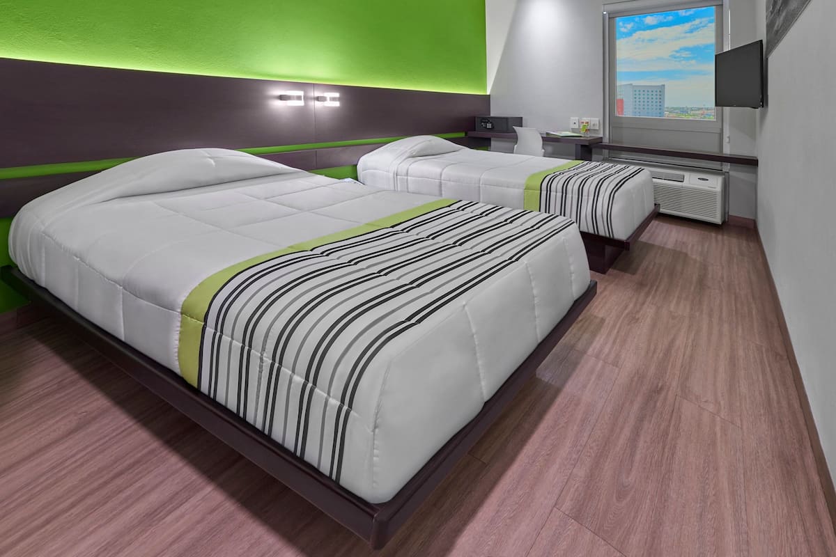 A modern hotel room with two beds, a desk, and a TV.