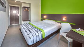 Una habitación de hotel moderna con una cama, un escritorio y una silla. Cuenta con una pared verde de acento y una puerta con interruptor de luz.