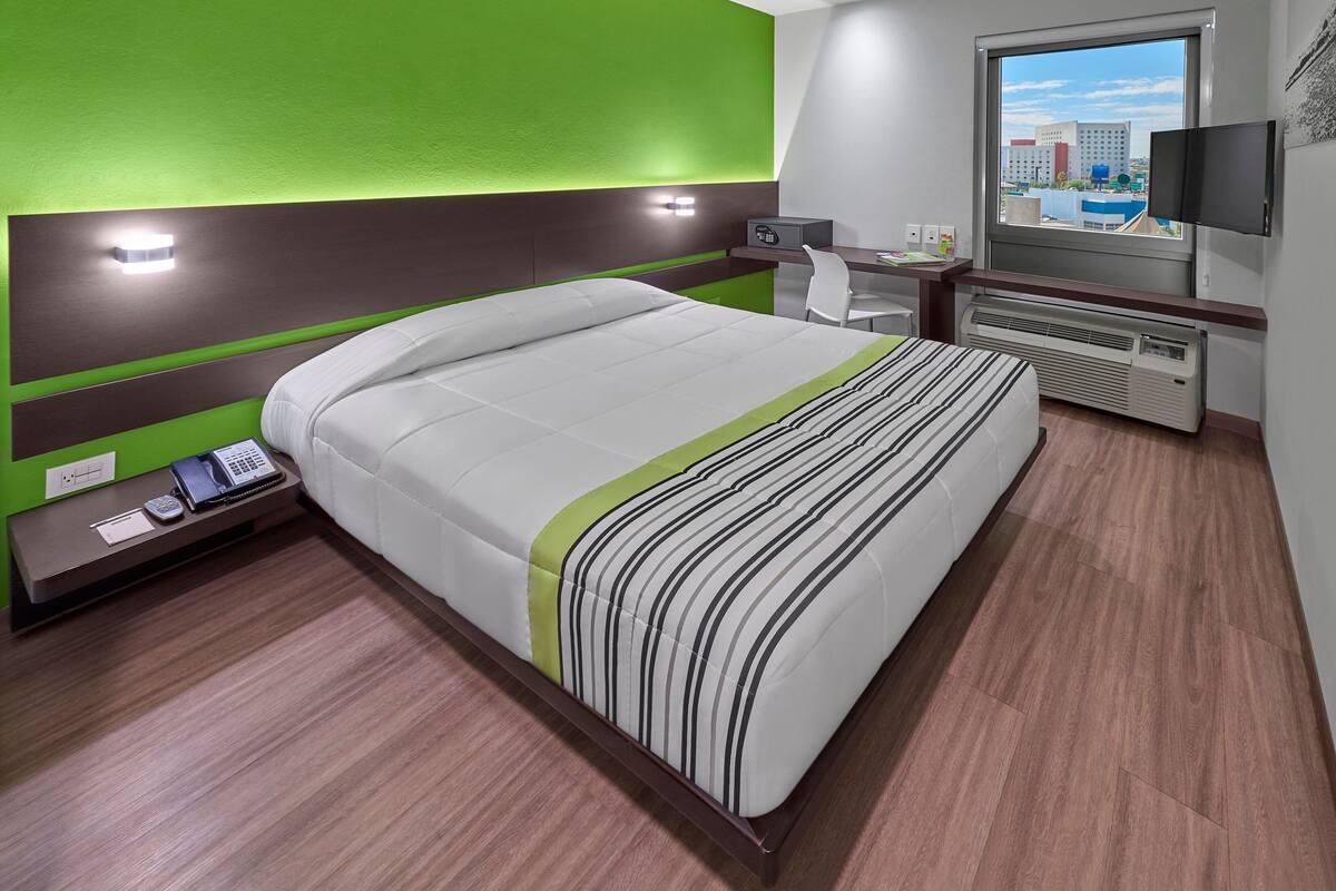 A hotel room with a bed, bedside table, desk, chair, TV, and a window with a city view.