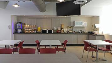 A modern kitchen with white cabinets, a microwave, and a coffee machine. There are red chairs and a white table in the dining area.