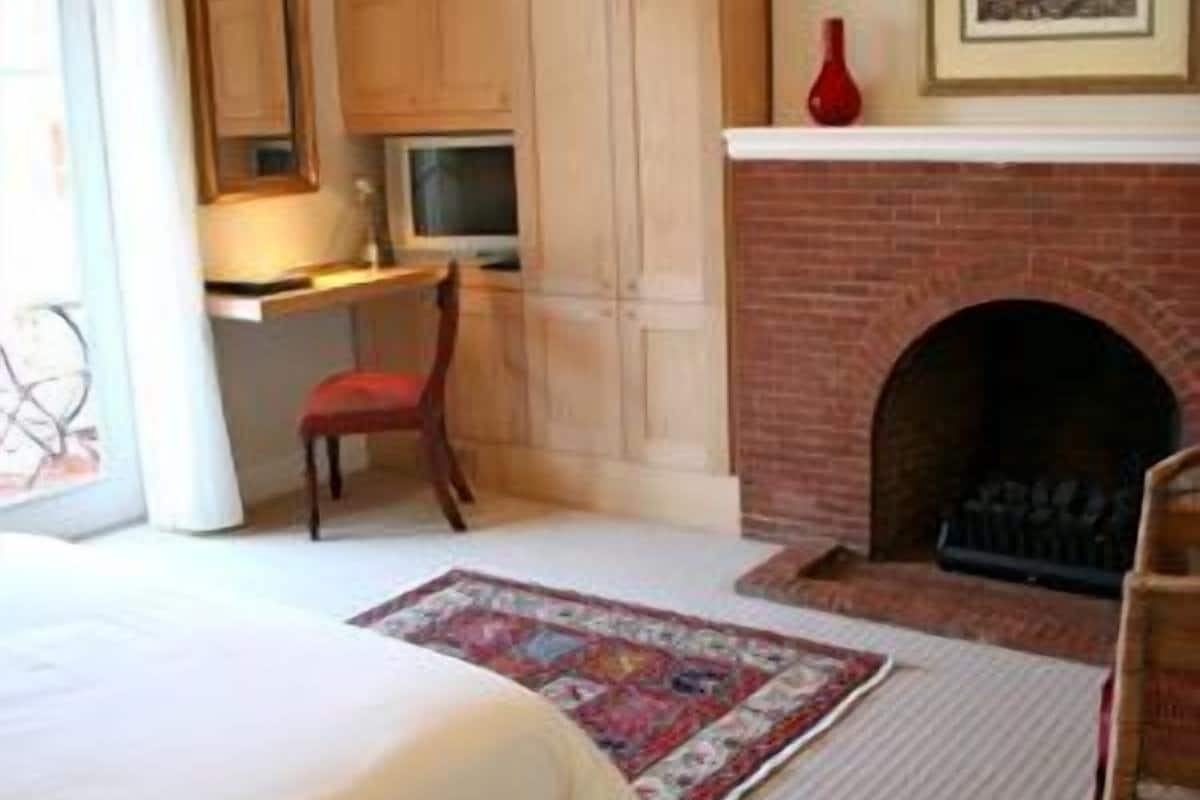A bedroom with a bed, a desk, a chair, a fireplace, and a rug.