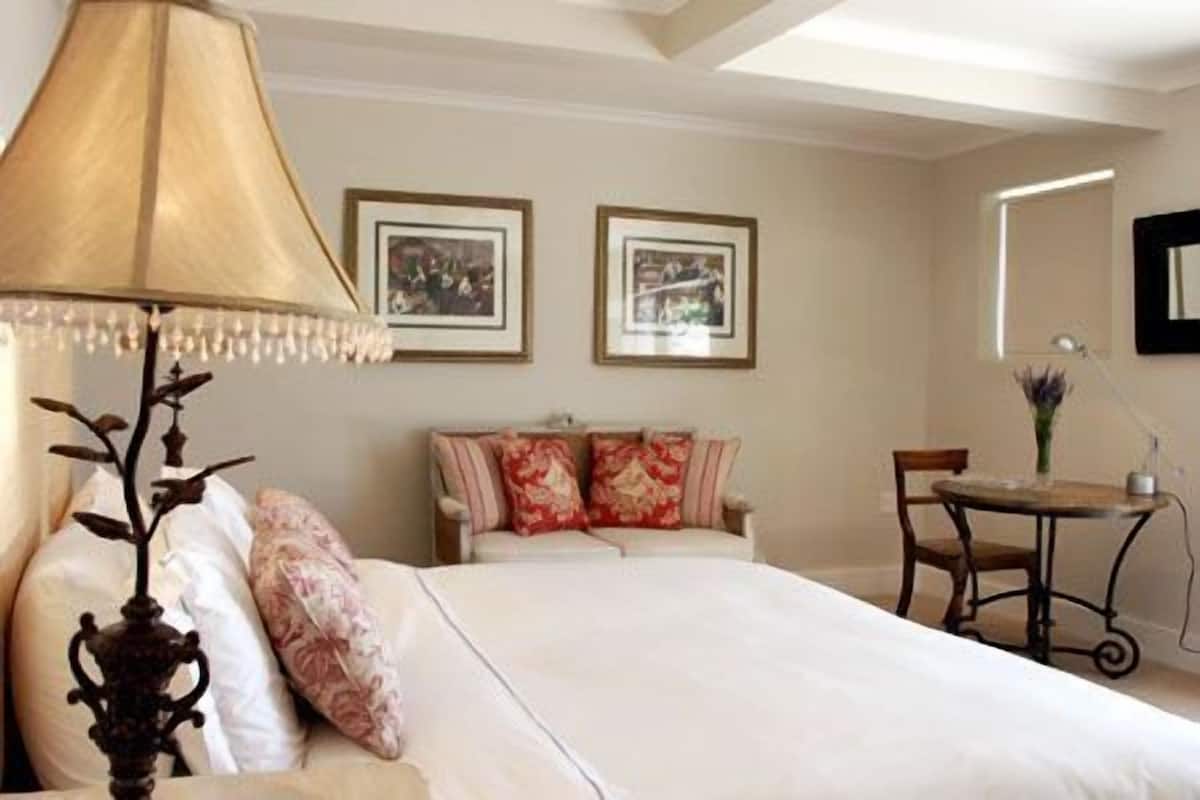 A hotel room with a bed, a bedside table with a lamp, a chair, and two framed pictures on the wall.