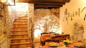 Un comedor rústico con paredes de piedra, una escalera de madera y una mesa para dos personas, con platos y cubiertos.