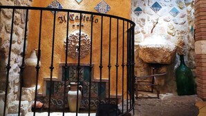 Una habitación con paredes de piedra, un mural, una barandilla metálica y un lavamanos de piedra.