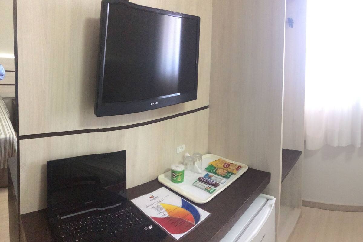 A hotel room with a bed, bedside table, lamp, and a TV mounted on the wall.