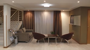 A living room with a sofa, two armchairs, a coffee table, a TV on the wall, and a staircase with a handrail. - Barigui Park Hotel (Curitiba)