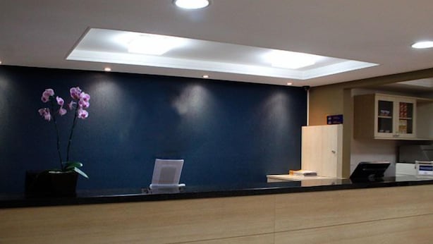 A reception area with a dark blue wall, a potted orchid, a desk with a laptop, and a small cabinet. - Barigui Park Hotel (Curitiba)